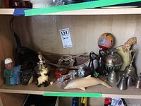 Shelf holding various pottery, ceramic, glass, and wood figurines, metal bells, a wooden indigenous model canoe, and trinket box.