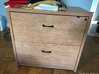 Front view of two-drawer laminate filing cabinet with lock on the top drawer and black handles, wood grain finish.