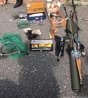 Overview of fishing rods, reels, tackle boxes, nets, and accessories laid out on asphalt.
