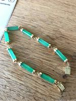 Full view of the gold and green stone bracelet laid flat on a wooden surface.