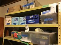 Shelf with boxes and plastic bins labeled as plumbing supplies including one marked Plumbers Lot.