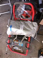 Overall front view of red tubular steel frame pressure washer with coiled hose and fabric bag strapped on top