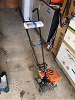 Full view of Echo TC210 tiller with attached handle, metal frame, tines and rolled manual strapped to handle