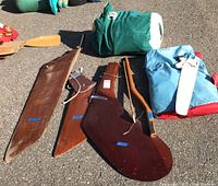 Photo showing three rudders/centre boards and two bagged sails arranged on pavement.