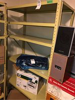 Front view of one metal shelving unit loaded with items and a speaker on the side.