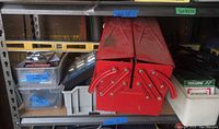 Shelf with red metal toolbox open, showing compartments, along with plastic containers, level and other tools on shelf