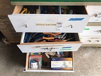 Three drawers open showing screwdrivers in top drawer, pipe wrenches and pliers in second drawer, and a Danze bathroom sink faucet with parts in third drawer.