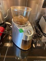 Side view of Capresso coffee grinder on kitchen counter showing stainless steel body and clear plastic bean container with ground coffee inside.
