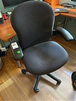 Full view of the black fabric office swivel chair with armrests on wood floor.