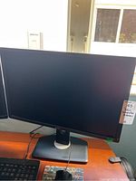 Front view of a 26 inch Dell computer monitor on a stand, screen off, placed on a desk near a window.