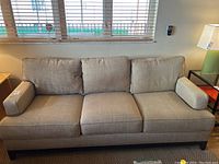 Front view of beige Ethan Allen sofa with three cushions beneath window