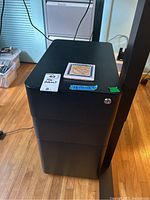 Front view of black metal file cabinet showing top surface, lock detail, and condition with scratches.