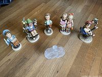 Group photo of six Hummel figurines and Lalique crystal perfume bottle on wooden floor