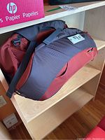 Side view of Osprey Porter 46 backpack showing red body and gray padded shoulder straps with carry handle on top.