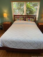 Full frontal view of queen size wooden platform bed with headboard, showing bedding and pillows.