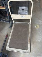 Metal platform dolly with rubber handle showing rust and dirt on platform surface.