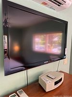 Front view of Samsung flat screen TV mounted on wall, showing entire screen and part of room reflection.