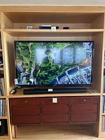 Front view of Sony Bravia TV displaying aerial scenery, soundbar below, remote on shelf