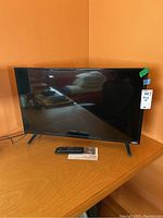 Front view of the 33-inch Vizio television on a wooden table with remote and manual in front of it.