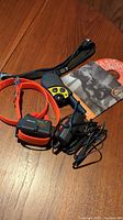 Photo of orange dog collar with black receiver labeled FR-300B connected to cables, handheld black and yellow remote control, and manual CD.