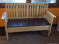 Front view of a wooden bench with a dark wooden seat and light wood frame with a slatted backrest and armrests