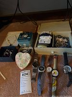 Full lot view showing wristwatches laid out with containers holding multiple costume jewelry items including necklaces, hair ties, barrettes.