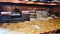 Wide photo showing Philips CD changer, Technics stereo receiver and cassette deck with stacks of CDs and cassette tapes on top.