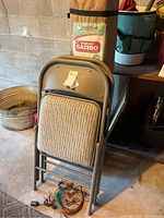 Original packaged 10x10 First-up gazebo bag with two beige padded metal folding chairs stacked in front