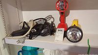 Two portable battery-operated flashlights and four extension power strips on white shelf; red flashlight, yellow Eveready flashlight, four power strips with cords
