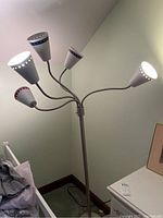 Full view of the silver floor lamp with five flexible gooseneck lights lit and visible from a corner showing height and design.