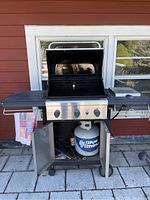 Front view of Kenmore gas grill with open cabinet door showing propane tank inside, grill has a flip top lid with a key hanging from the handle.
