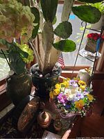 Live cactus in green vase and faux hydrangea vase on table near window with various decorative items