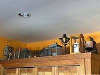 Top shelf showing a variety of metal and glass oil lamps and candle holders arranged in a row against an orange wall