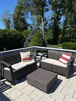 Overall outdoor patio set with two loveseats, ottoman, cushions, and decorative pillows on paved deck.