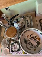 Photo showing tea kettle, candle stick holders, salt and pepper shakers, coasters, butter dish, and other ceramic items with botanical pattern