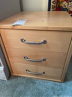Closed wooden storage box with three wooden drawers and metal handles shown from front.
