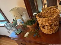 View of the wooden table holding blue metal Better Homes & Gardens fan, floral lamp with white shade, potted trailing plant, and wicker basket.