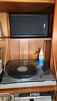 Photo showing the Technics SL-Q200 turntable with clear plastic dust cover and a vinyl record on the platter with record cleaner bottle beside it.