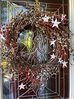 Grapevine wreath decorated with white and red berries and white five-pointed star ornaments hanging on a glass door.