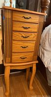 Full front view of wooden standing jewelry case showing five drawers with metal decorative handles and carved front panels.