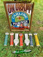 Frontal photo of Carling Pilsener mirror and six beer tap handles on grass