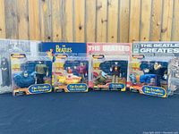 Four sealed Beatles Yellow Submarine collectible figures in original packaging displayed side by side with Beatles album covers in the background.