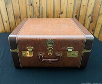 Closed brown hard case with leather handle, brass hardware, labeled 'Titano'.