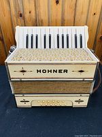 Front view of Classic Pearl Hohner accordion showing 15 white keys, decorative front panel with 'HOHNER' branding, and striped fabric bellows.