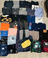 Overview of the clothing lot laid out on floor showing variety of shirts, pants, and accessories