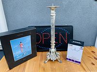 Photo showing the Pink Floyd box set, LED OPEN sign, D-Link device box, and ornate candlestick holder on a wooden table against a gray wall.