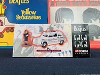 Front view of unopened box showing Beatles Collection branding, white taxi model with Beatles newspaper print, and driver figure inside display window