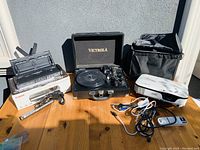 Full view of lot showing Canon printer on box with power cable, Victrola turntable, Epson projector in black case, cables and remote controls on wooden table