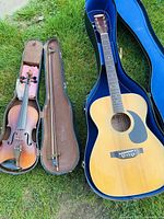 Acoustic guitar and violin side by side in open cases on grass
