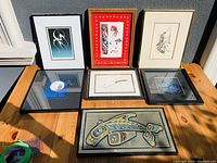 Full view of the six framed Indigenous art pieces laid out on wooden table, showing variety in colors and frames.